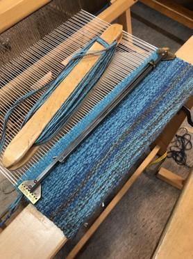 Kuvassa on pienoiskangaspuihin aloitettu kutomaan villaista penkinpäällistä. Väreinä on käytetty turkoosia, sinistä ja harmaata. Työvälineinä näkyy puinen sukkula ja metallinen pingotin.